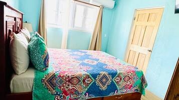 A bedroom with a wooden bed, a ceiling fan, a window with curtains, and a wooden door.