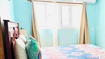 Una habitación con cama, ventilador de techo, ventana con cortinas y aire acondicionado.