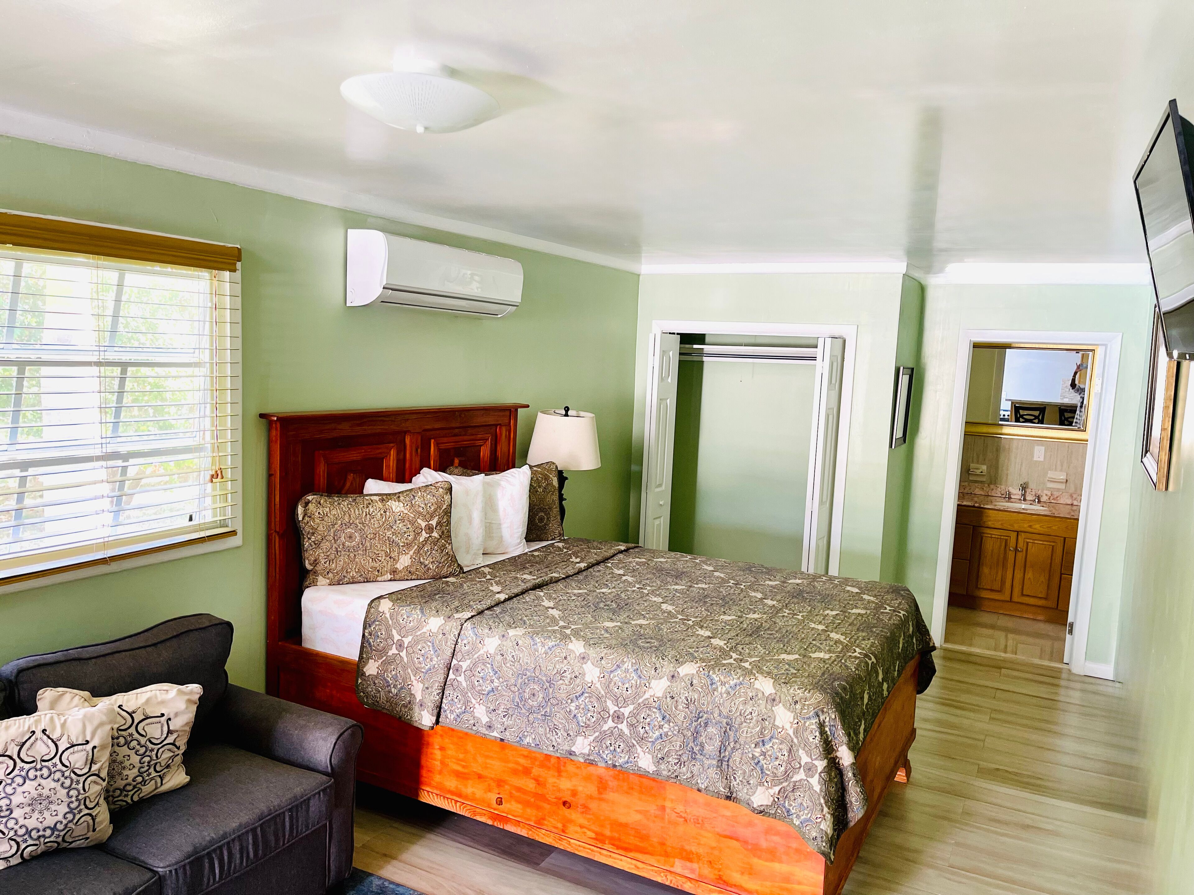 Une chambre à coucher avec un lit, une table de chevet avec une lampe, une armoire et une salle de bain visible à travers une porte ouverte.