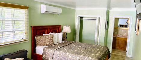 Une chambre à coucher avec un lit, une table de chevet avec une lampe, une armoire et une salle de bain visible à travers une porte ouverte.