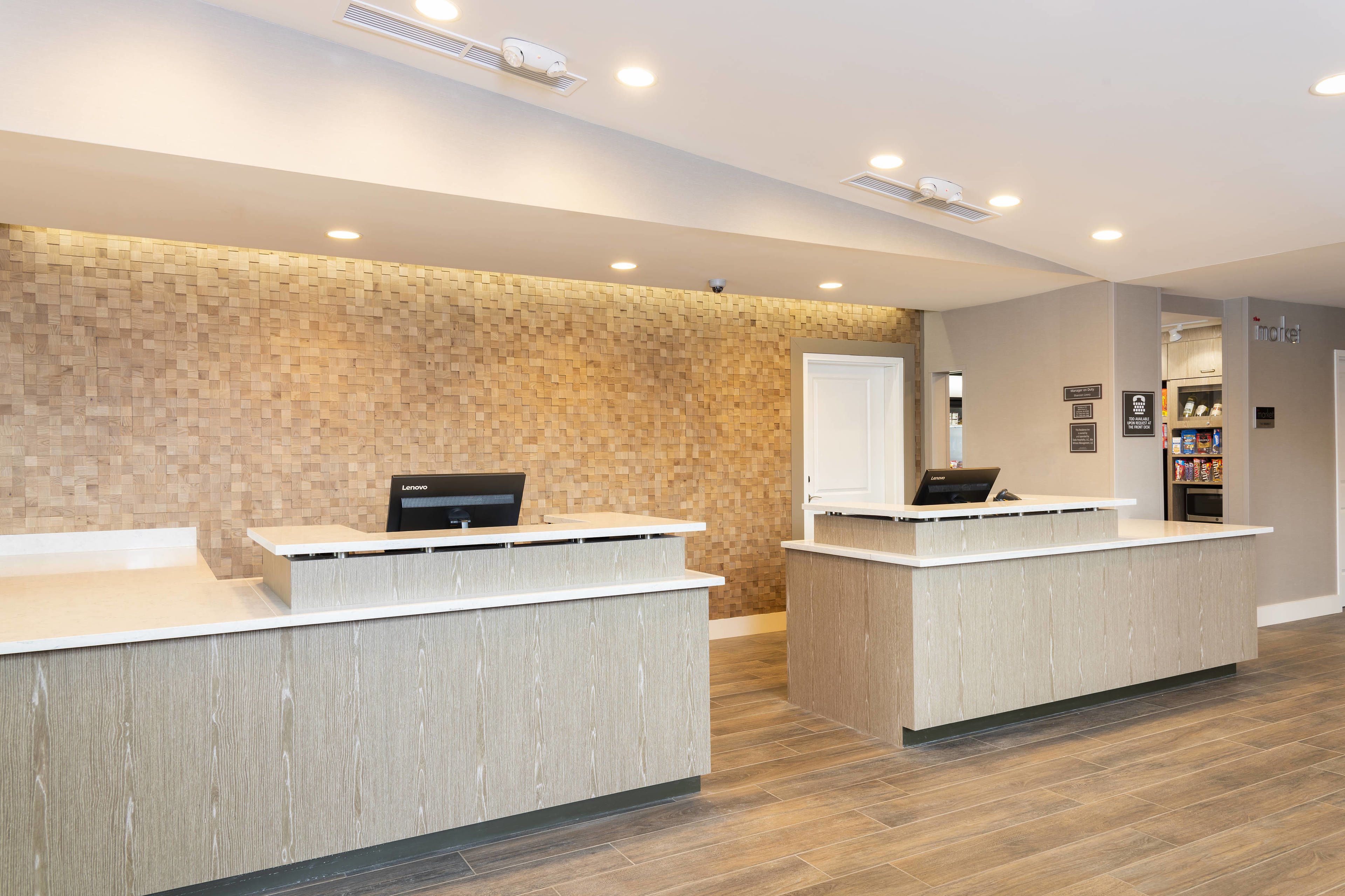 A reception area with two reception desks, a wall with a mosaic pattern, and a door leading to a kitchenette.