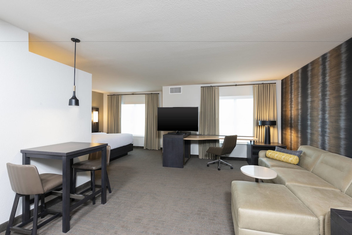 A hotel room with a bed, a desk, a TV, a sofa, and a small table.