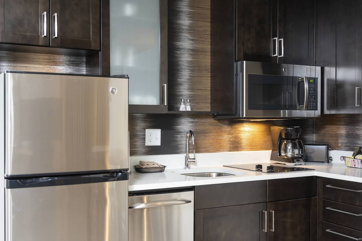 A modern kitchen with stainless steel appliances, dark wood cabinets, and a white countertop.