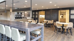 A modern dining area with a long wooden table and multiple chairs, a kitchen area with appliances, and a bar area with stools. - Residence Inn by Marriott Lafayette (Lafayette)