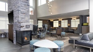A spacious lounge area with a stone fireplace, comfortable seating, and a large window providing natural light. - Residence Inn by Marriott Lafayette (Lafayette)