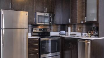 Una cocina moderna con electrodomésticos de acero inoxidable, armarios de madera oscura y encimera blanca.