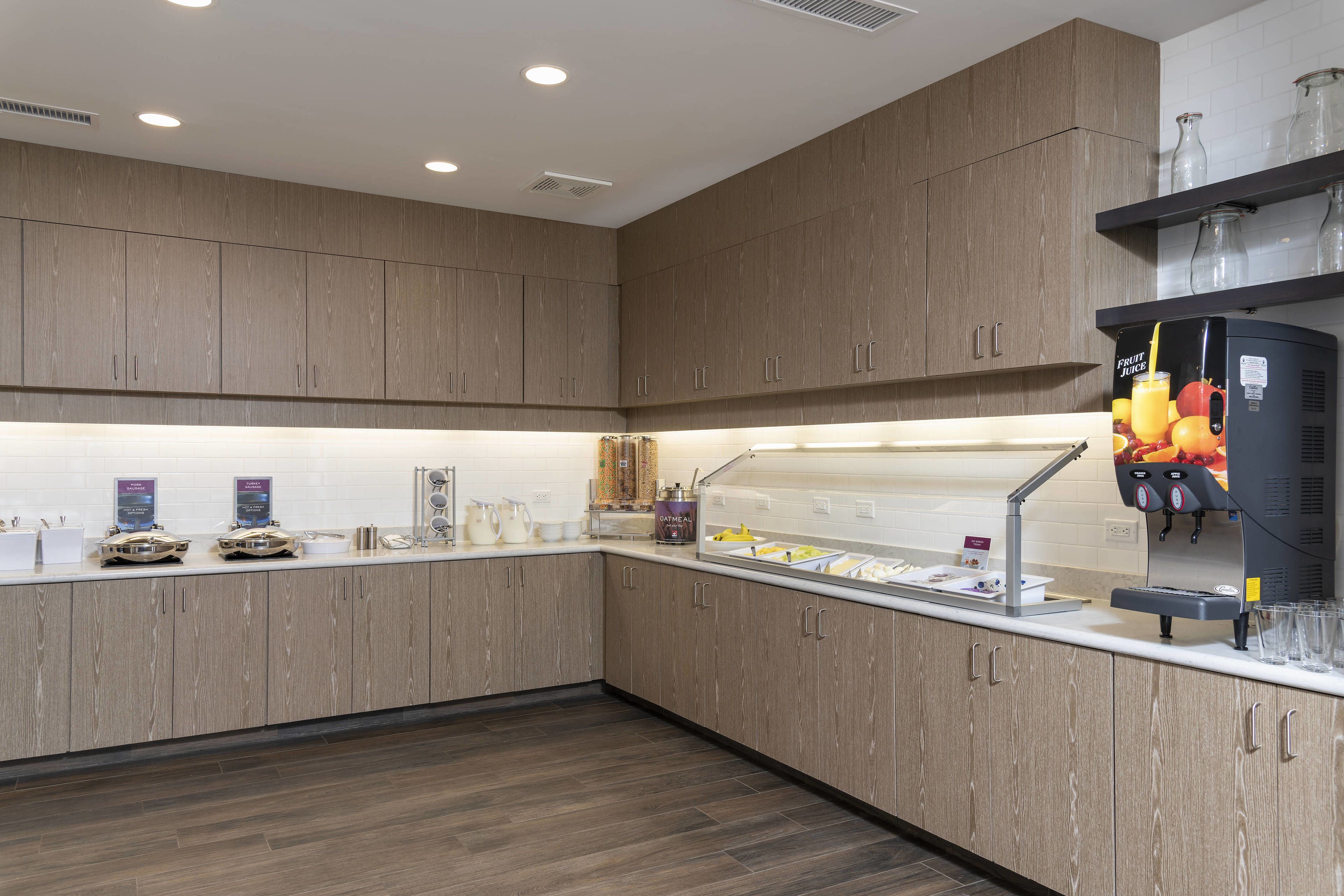 A modern kitchen with wooden cabinets, a fruit juice dispenser, and a coffee machine.