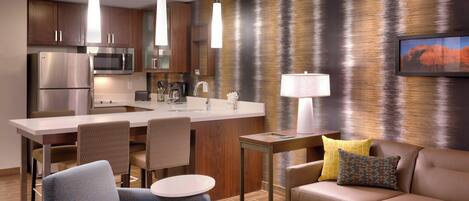 Quarto de hotel moderno com cozinha compacta, área de refeições, sofá e luminária.