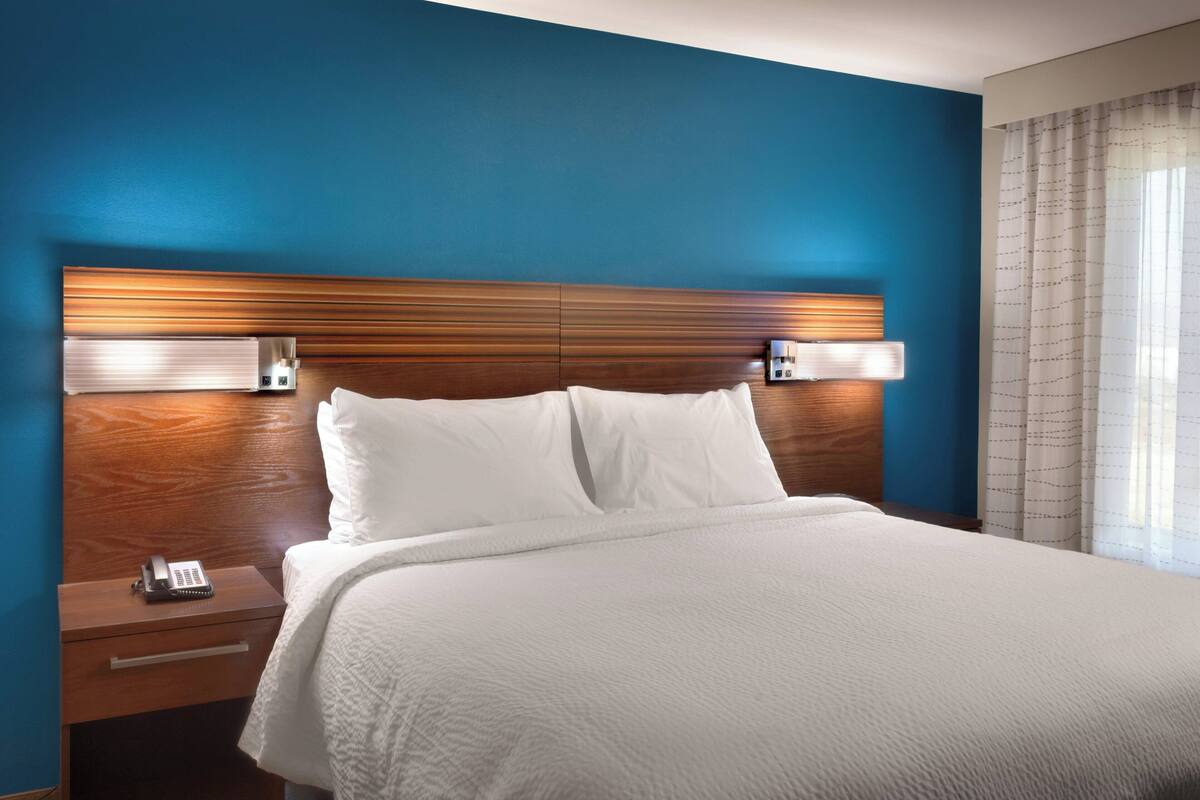 Une chambre d’hôtel avec un grand lit, une tête de lit en bois, des lampes de chevet, une table de chevet et un téléphone.