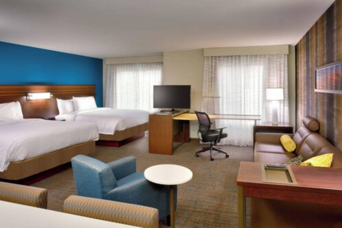 Une chambre d’hôtel avec deux lits, un bureau avec un ordinateur, une chaise, un canapé et une petite table.
