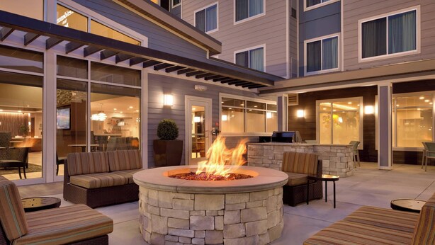 Un patio al aire libre con una chimenea de piedra, asientos y una sección cubierta con puertas de vidrio.