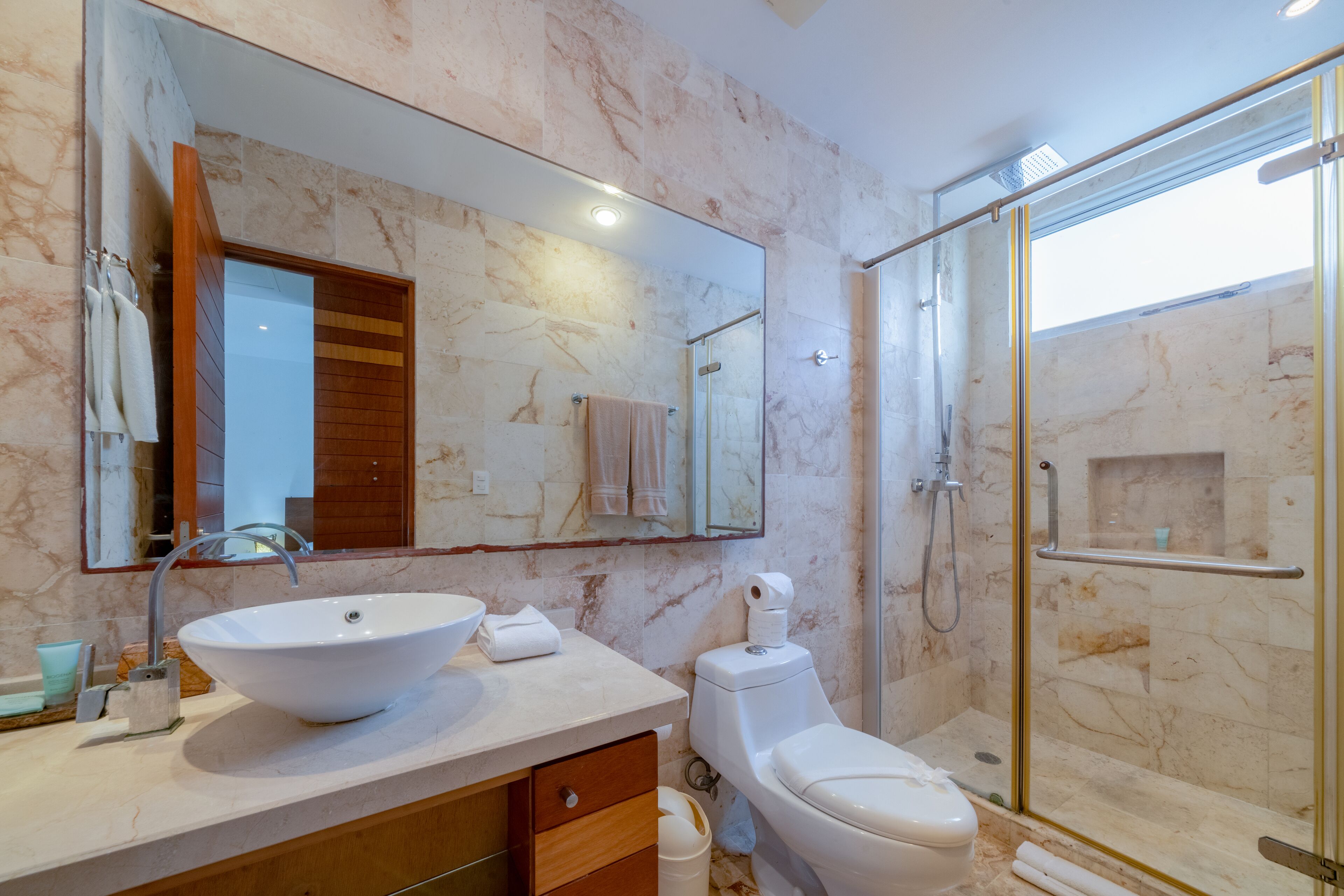 A modern bathroom with a large white sink, a toilet, and a glass-enclosed shower.