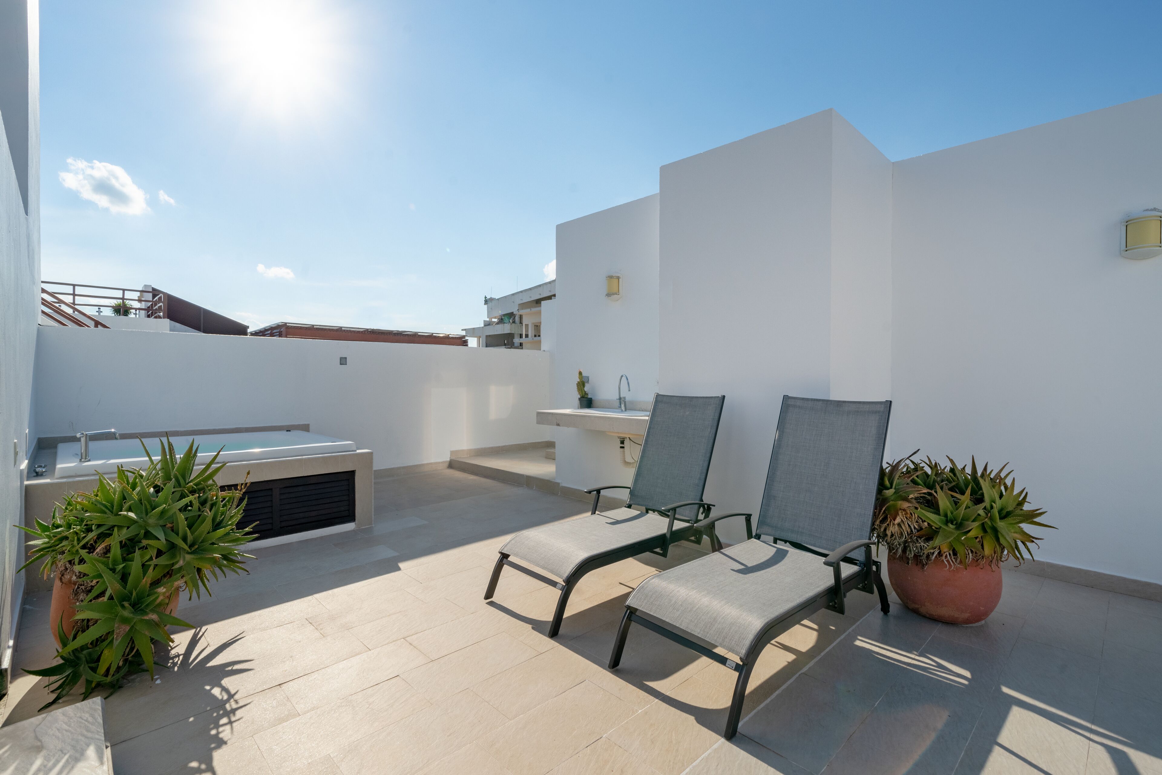 A rooftop terrace with two chairs, a small table, a potted plant, and a pool.