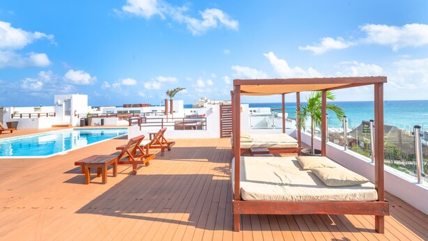 A wooden deck with a pool, lounge chairs, and a bed with a canopy overlooking the ocean. - Turquesa by NAS (Playa del Carmen)