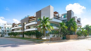 A modern multi-story hotel with a prominent entrance, palm trees, and a clear blue sky. - Turquesa by NAS (Playa del Carmen)