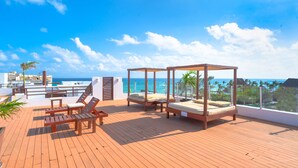 A wooden deck with a bed, lounge chairs, and a table overlooking the ocean. - Turquesa by NAS (Playa del Carmen)