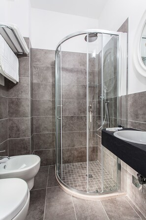 Un baño moderno con ducha de vidrio, encimera negra y dos inodoros blancos.