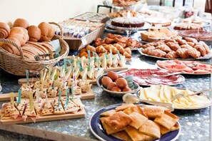 Una mesa de buffet con diferentes opciones de comida, incluyendo panes, pasteles y sándwiches.