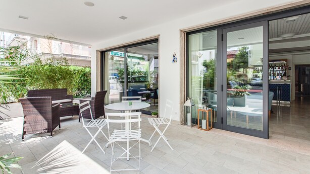 Un patio con mobiliario de mimbre, una mesa redonda y un ventanal de vidrio que da a una cocina.