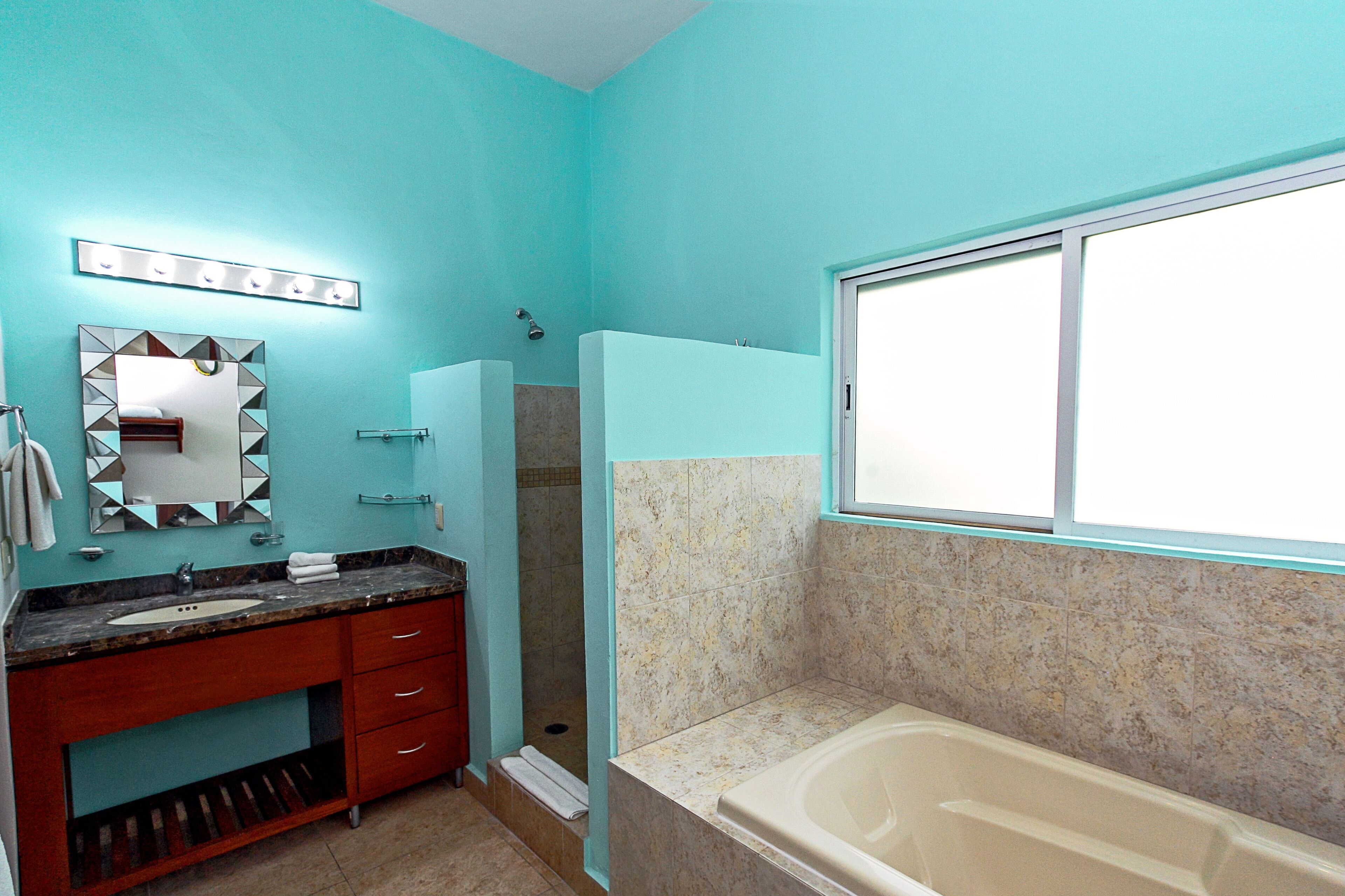 Un baño con una pared turquesa, un lavabo con un espejo encima, una zona de ducha y una bañera.