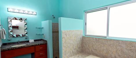 Un baño con una pared turquesa, un lavabo con un espejo encima, una zona de ducha y una bañera.