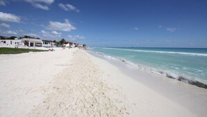 A beach with white sand and clear blue water. There are buildings along the shore. - Vista del Mar by NAS (Playa del Carmen)
