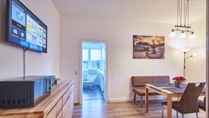Ein modernes Wohnzimmer mit Flachbildfernseher, Holzmöbeln, einem Esstisch und einem Gemälde an der Wand.