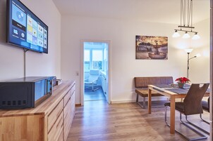 Una sala de estar moderna con un televisor de pantalla plana, muebles de madera, una mesa de comedor y un cuadro en la pared.
