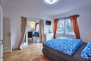 Un dormitorio con cama, una ventana con cortinas, un radiador y una puerta que da a otra habitación.