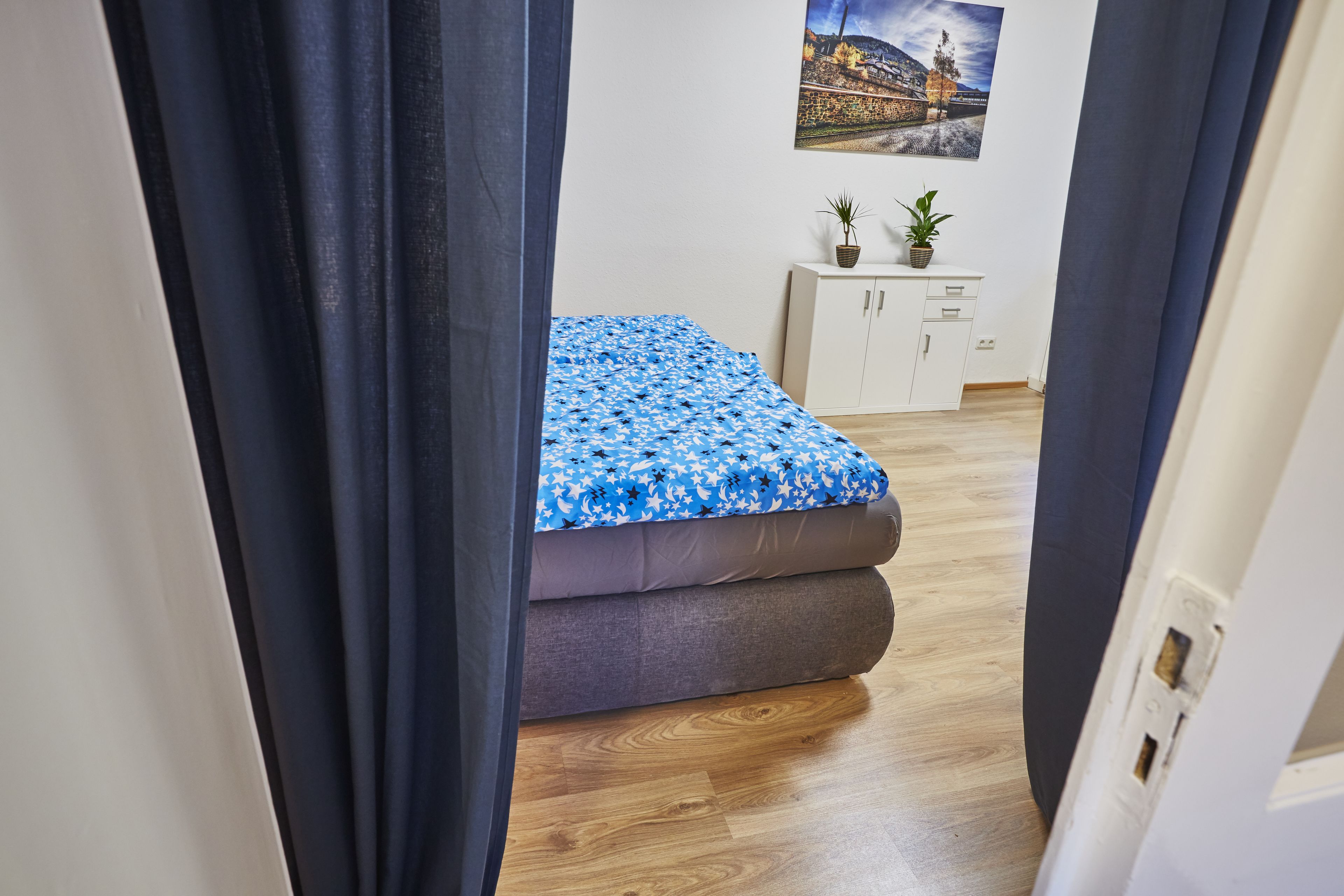 A bedroom with a bed, wooden flooring, a white cabinet, and a wall-mounted picture.