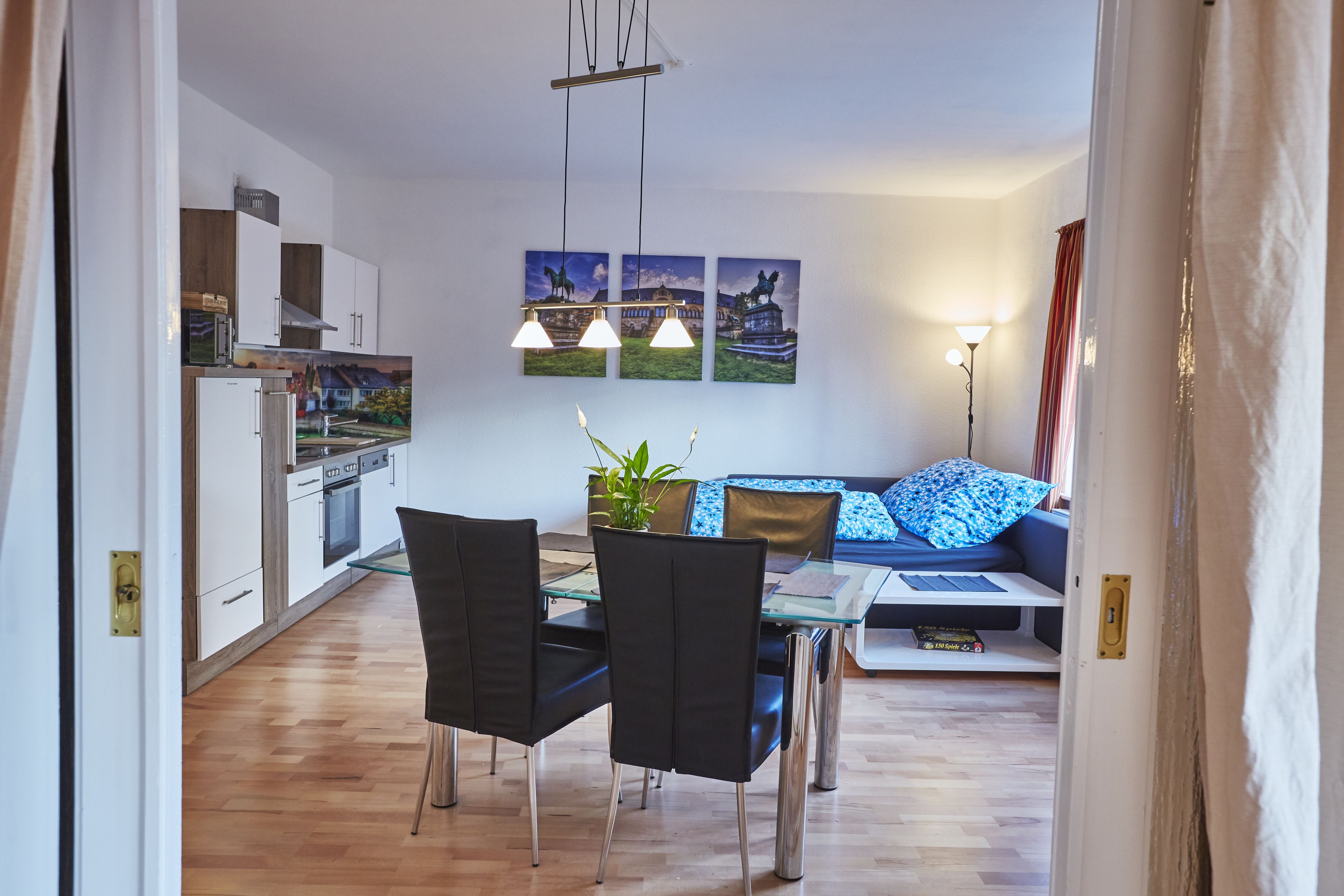 Une cuisine moderne avec des meubles blancs, une table à manger entourée de chaises noires et un canapé bleu agrémenté de coussins à motifs.