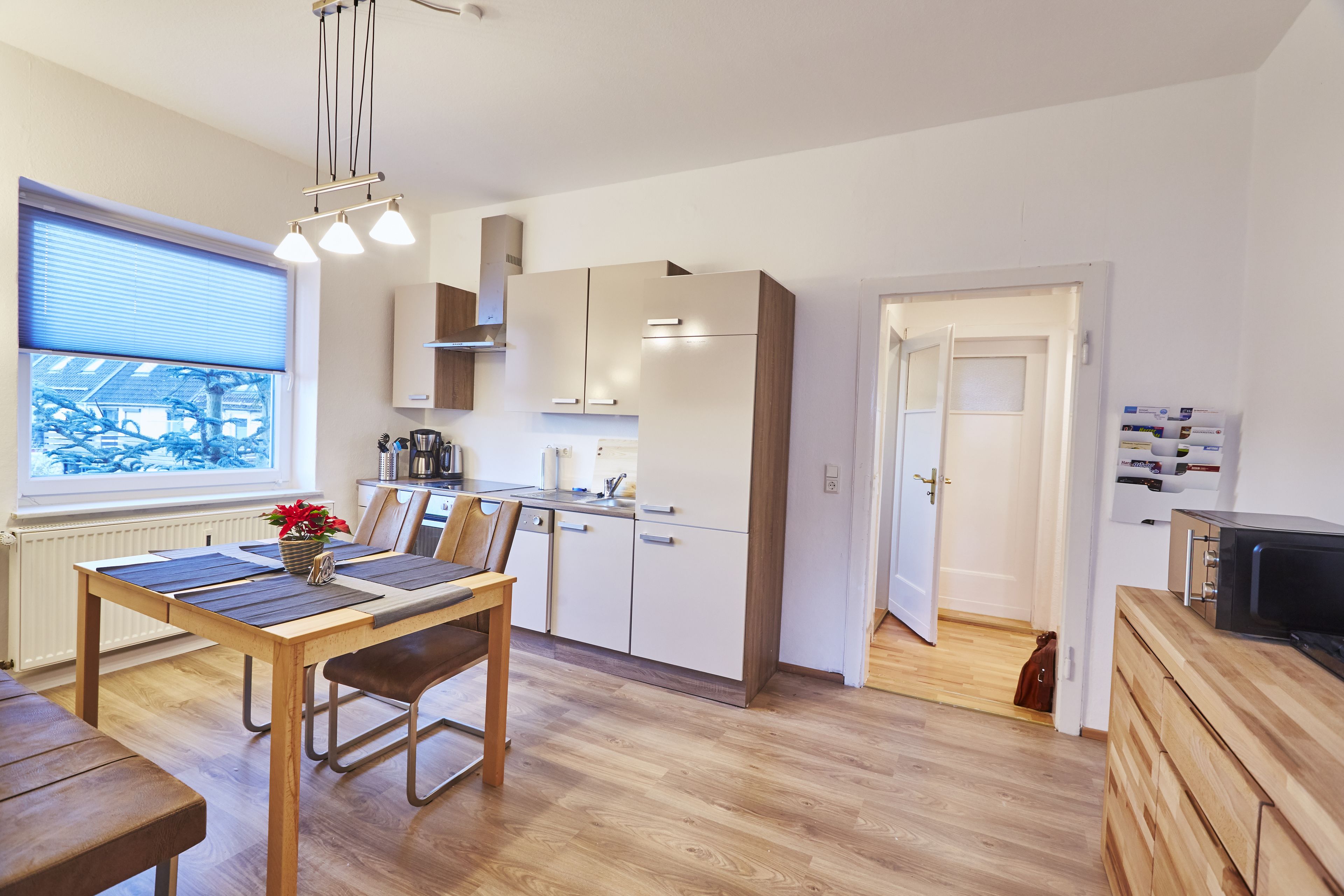 A modern kitchen with wooden cabinets, a dining table with benches, and a view through a window.