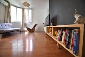 A living room with a sofa, a wooden bookshelf, and a television. - Depto Santiago 965 (Santiago)