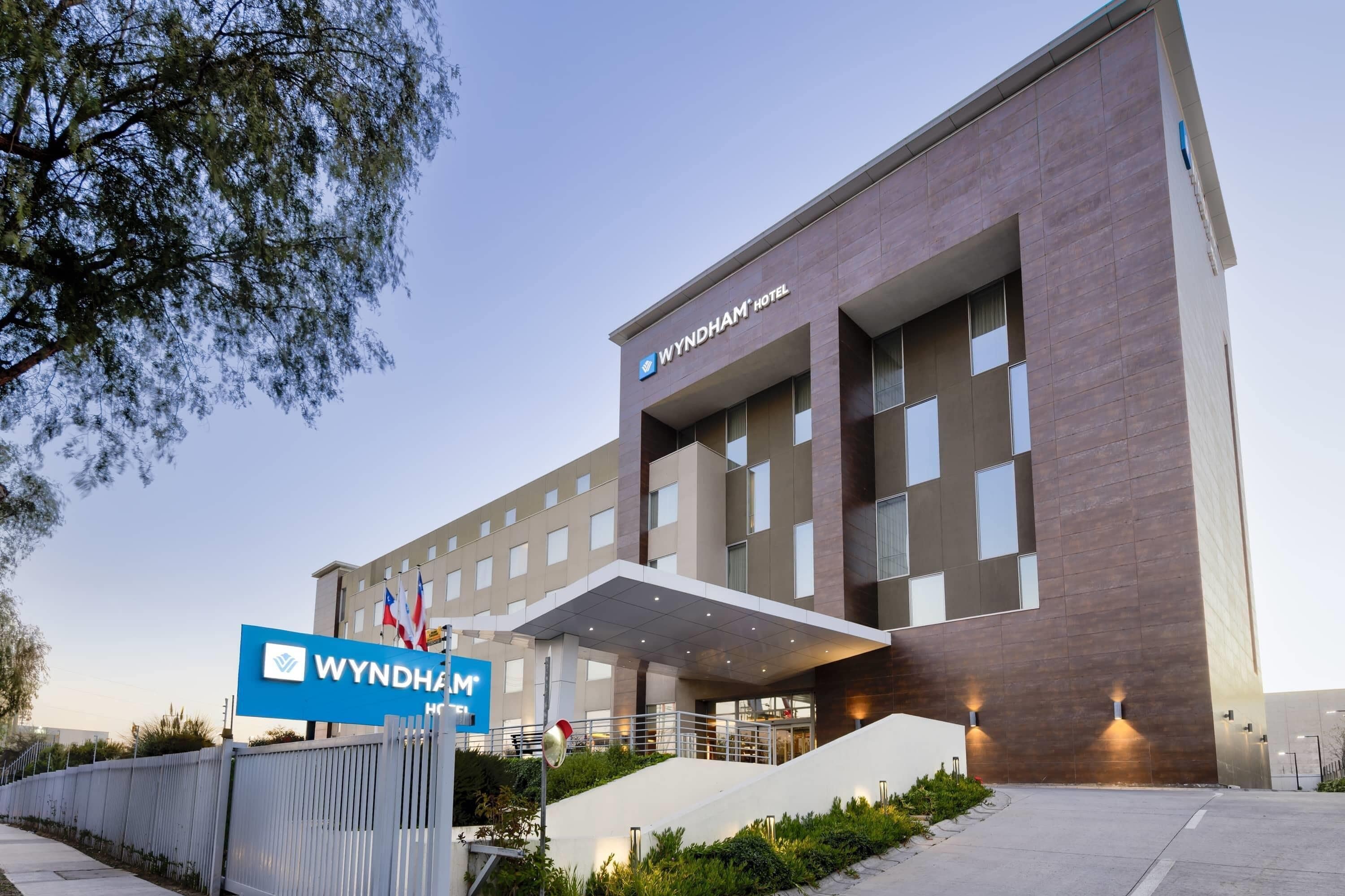 A modern Wyndham hotel building with a prominent entrance, a covered walkway, and a flag display.