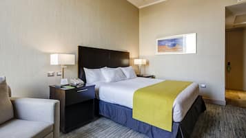 Habitación de hotel con cama, mesitas de noche, una silla, un cuadro en la pared y suelo alfombrado.