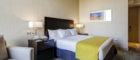 A hotel room with a bed, bedside tables, a chair, a painting on the wall, and a carpeted floor.
