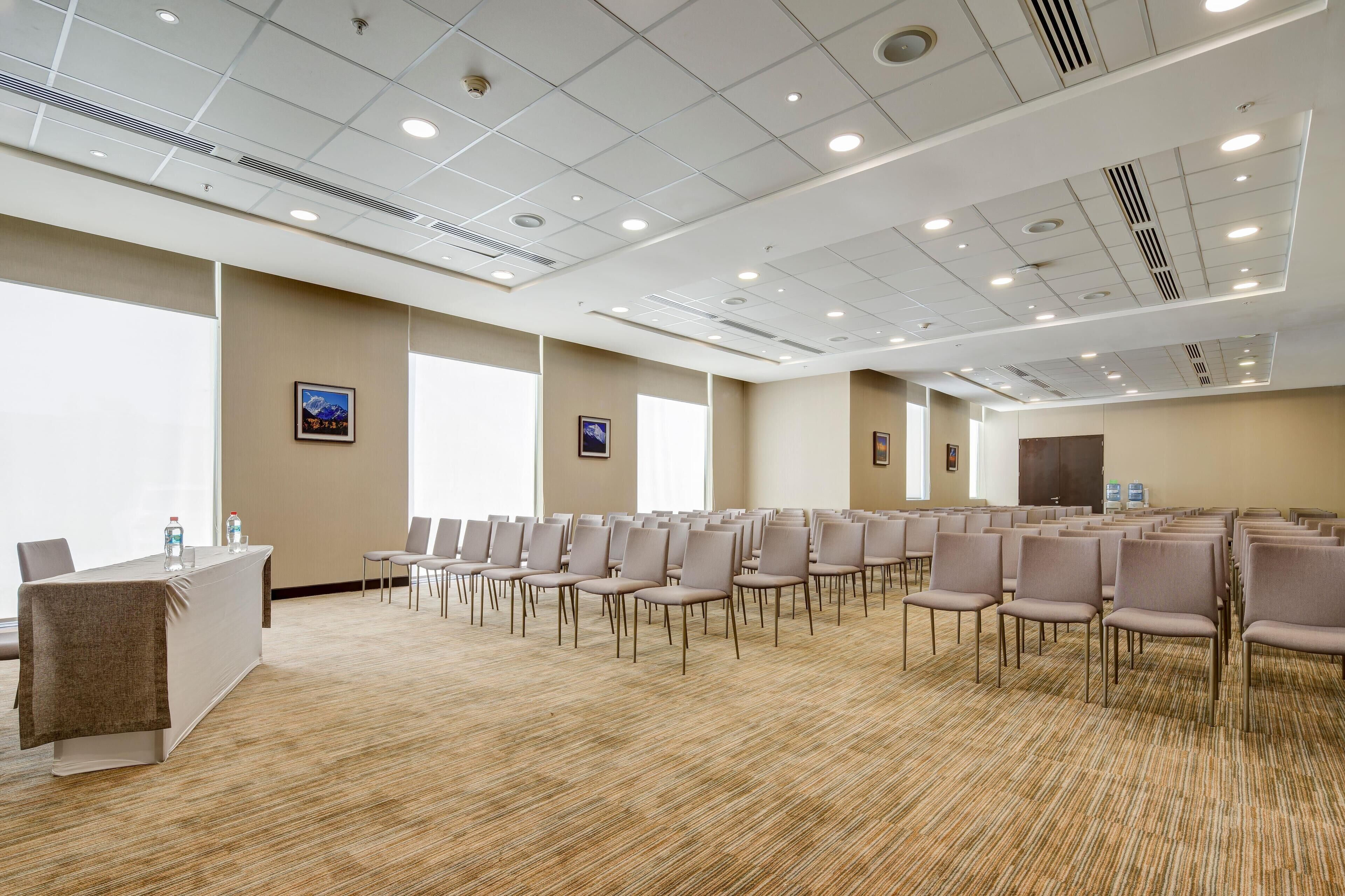 A conference room with rows of chairs, a table with a cloth, and framed pictures on the walls.