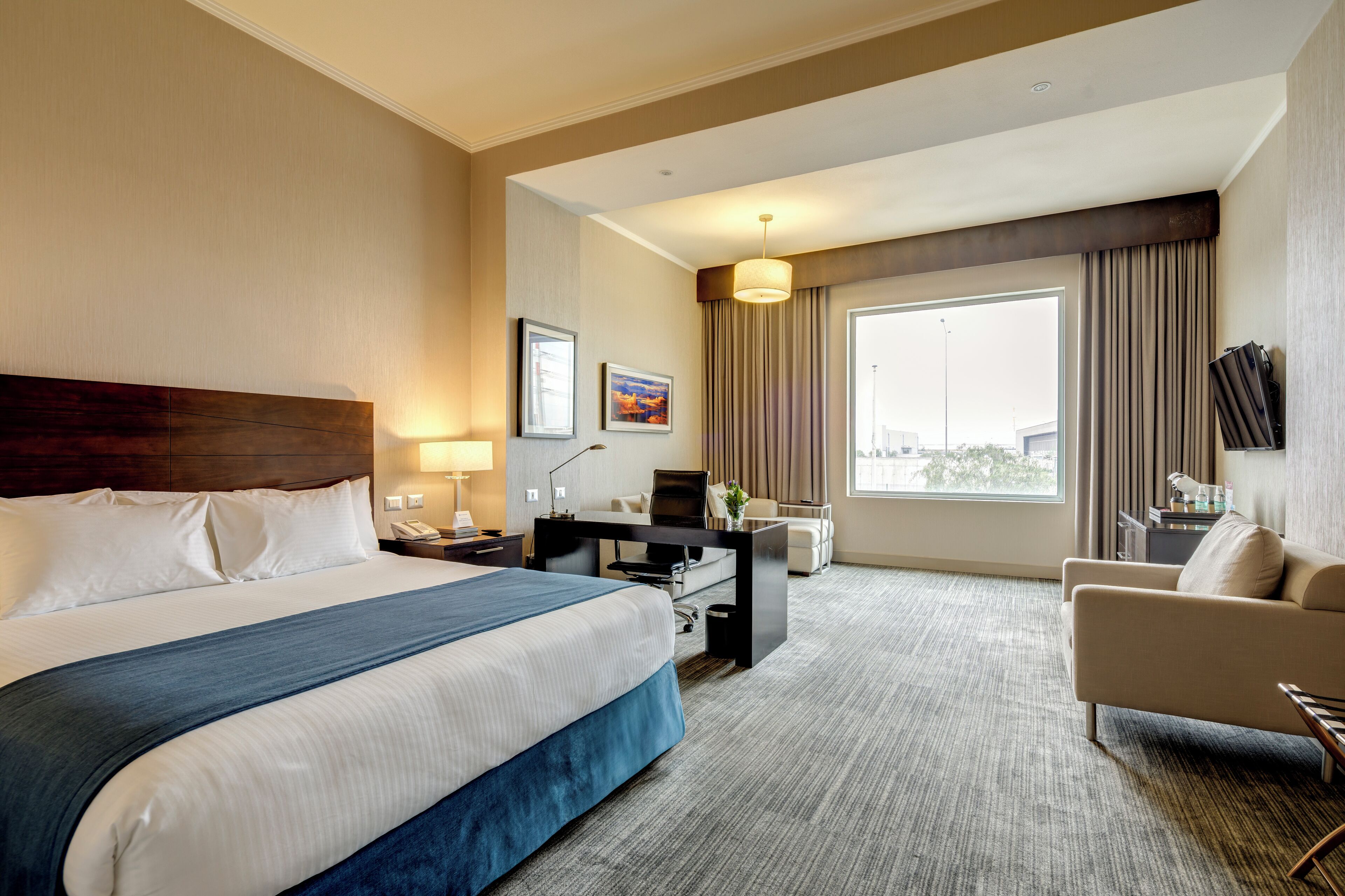 A hotel room with a large bed, a desk, a chair, and a large window.