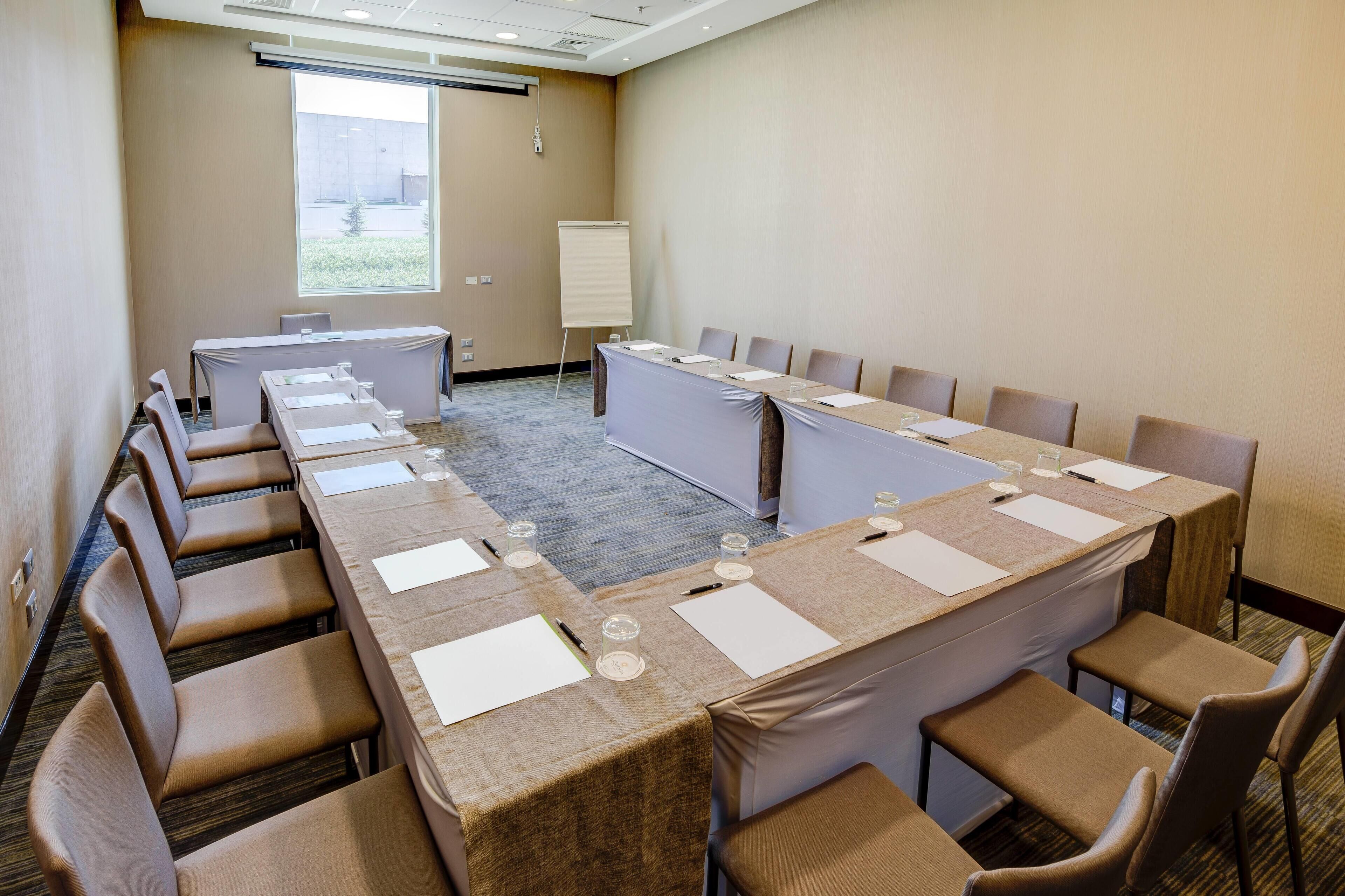 Un salón de conferencias con una larga mesa, sillas, una pizarra y un ventanal.