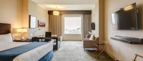 Habitación de hotel con una cama grande, un escritorio, una silla, un televisor y una ventana con cortinas.