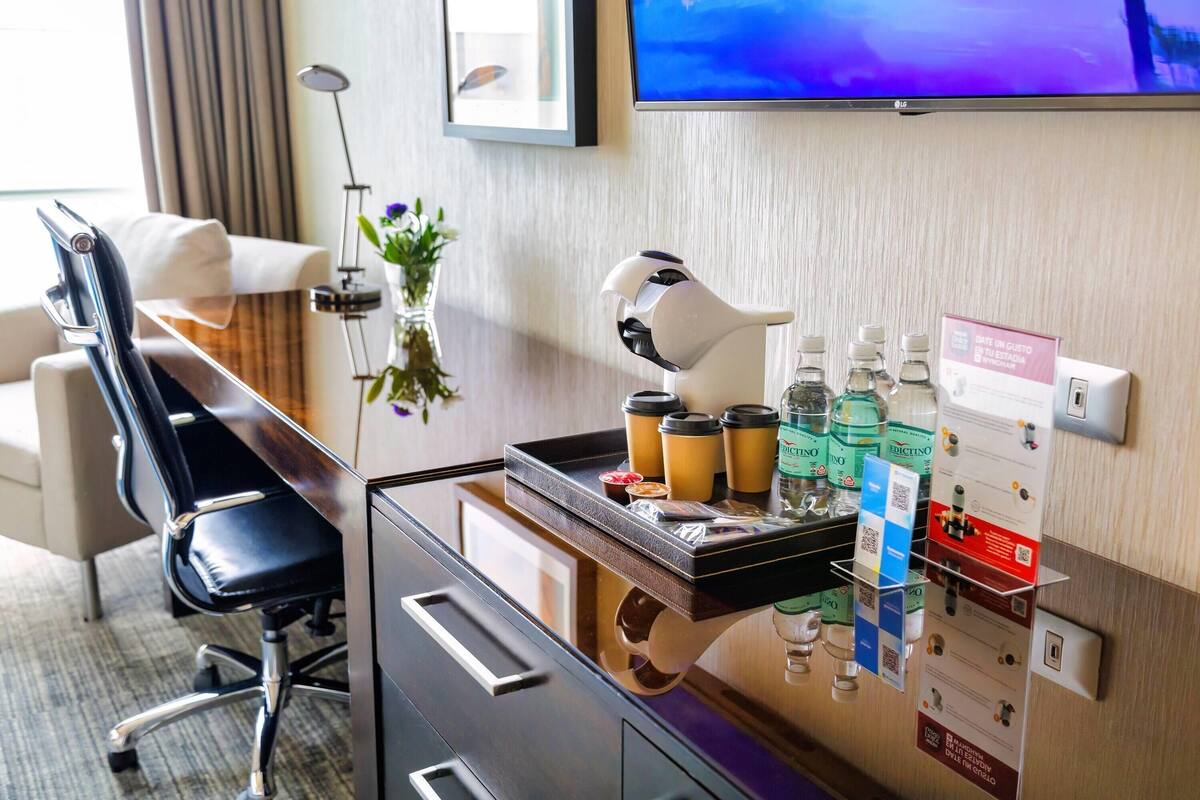 Un comptoir d’accueil d’hôtel avec un coin café, un téléviseur fixé au mur et une lampe de bureau.