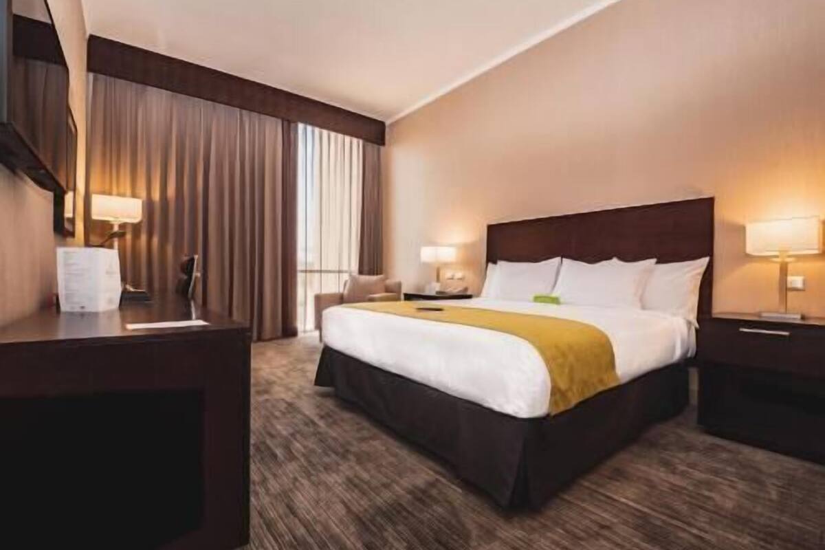 A hotel room with a bed, bedside tables, a desk, and a window with curtains.