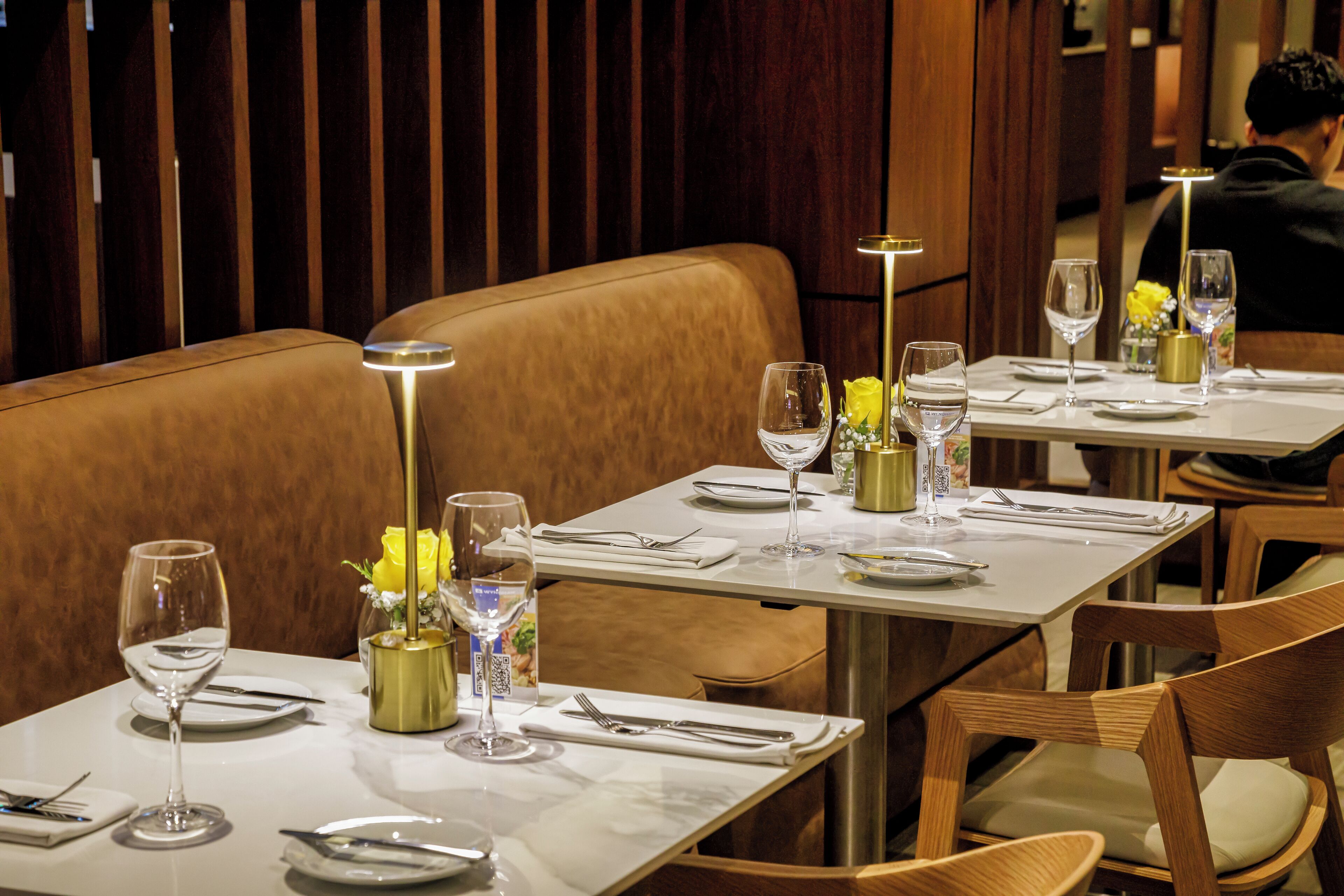 A restaurant interior with booths, tables set with white tablecloths, and gold accents.