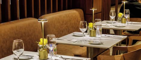 A restaurant interior with booths, tables set with white tablecloths, and gold accents.