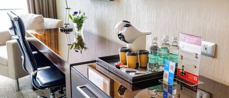 Una recepción de hotel con un televisor de pantalla plana, una máquina de café y varias comodidades como agua embotellada y un código QR para el registro digital.