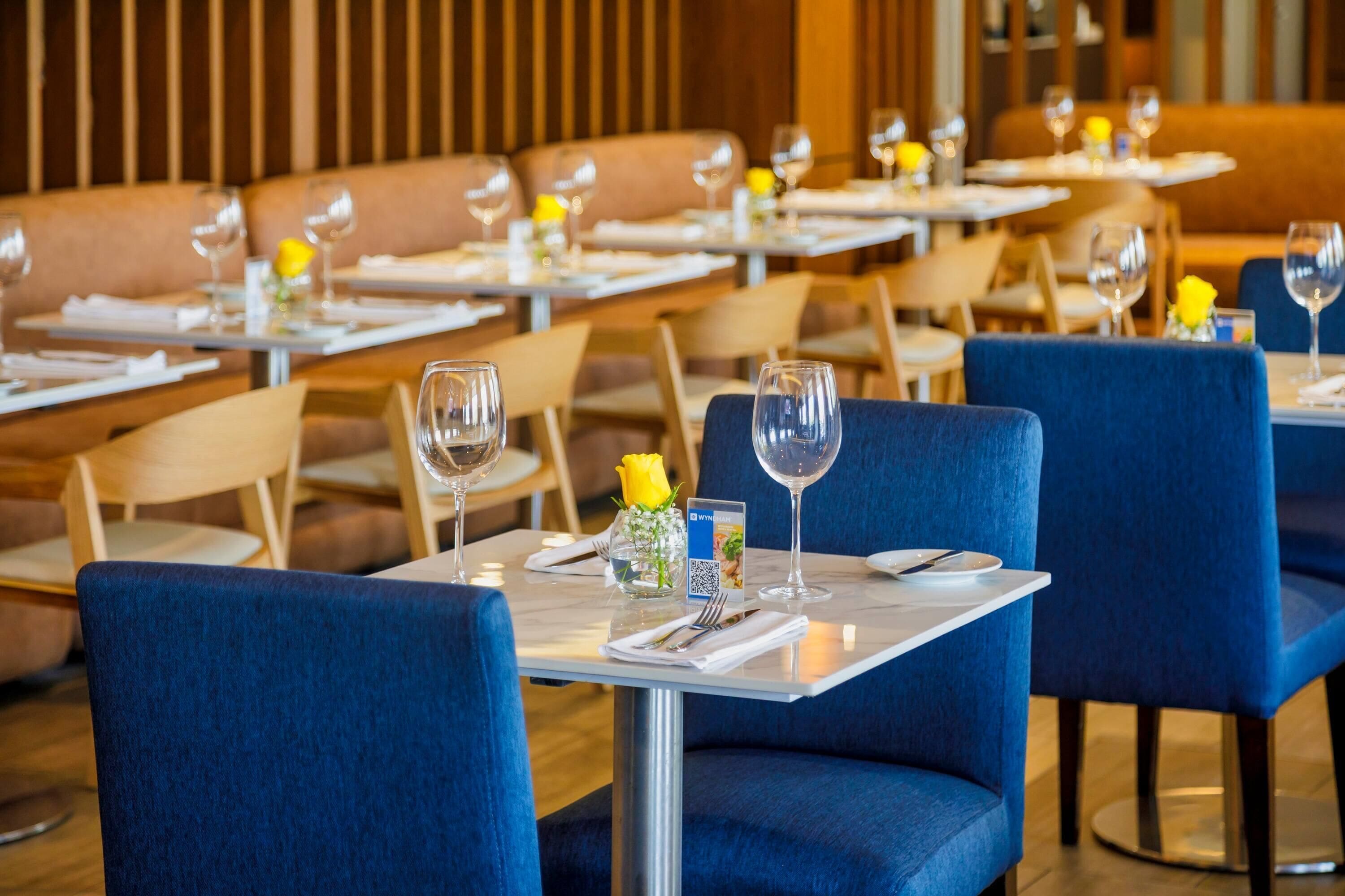 A restaurant with blue upholstered booths, white tables, and wine glasses set.