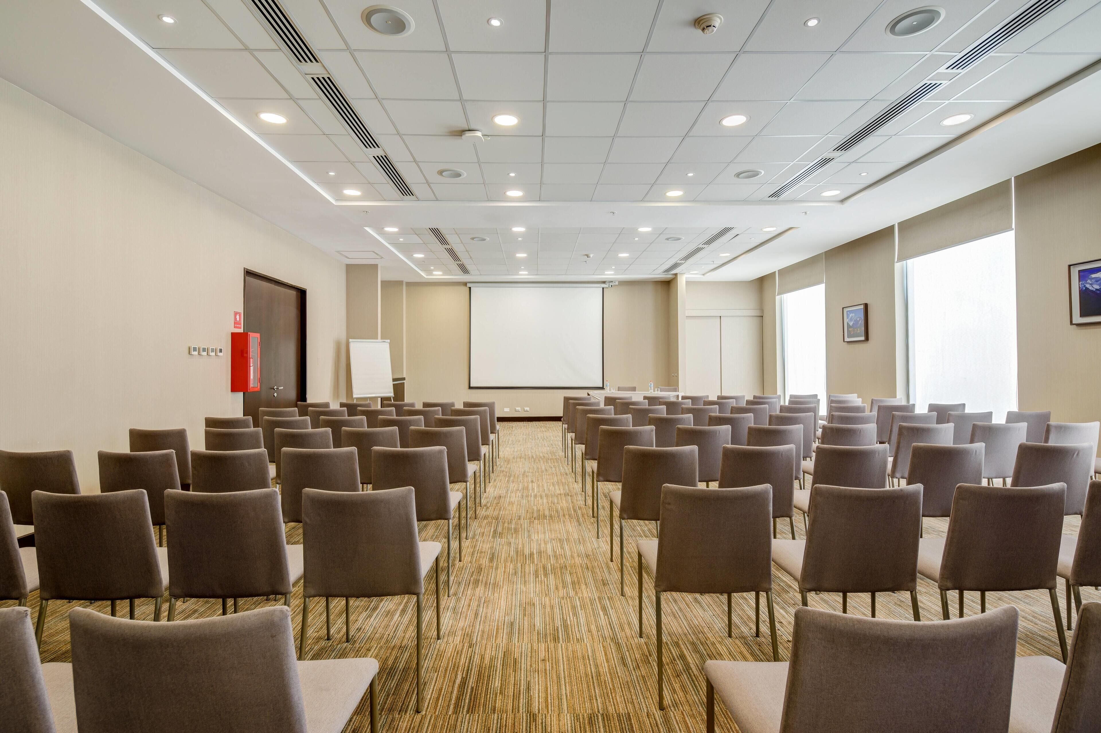 Ein Konferenzraum mit Reihen von Stühlen, einer Projektionsleinwand und einem Teppichboden.