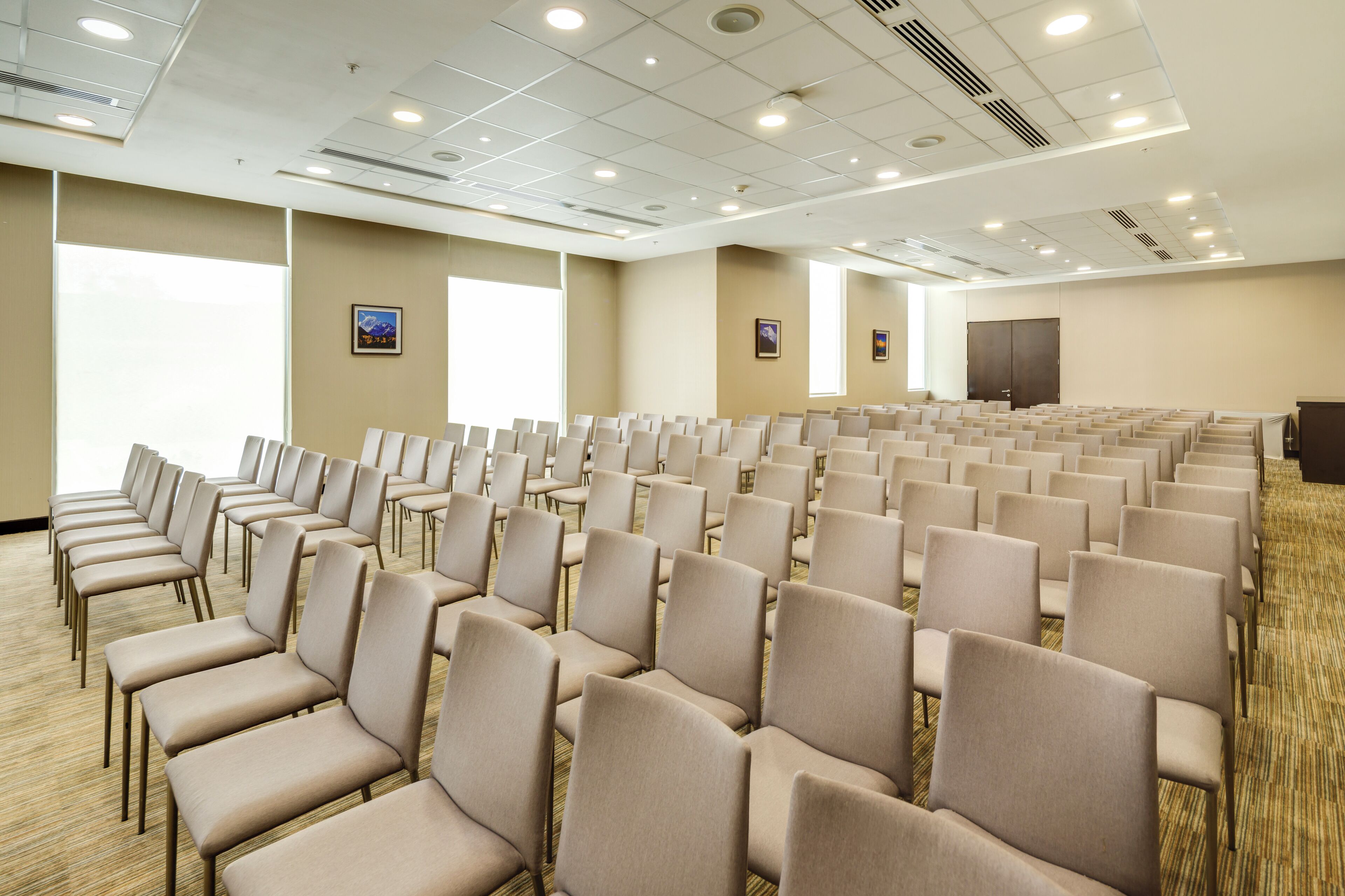 A conference room with rows of beige chairs, large windows, and a carpeted floor.