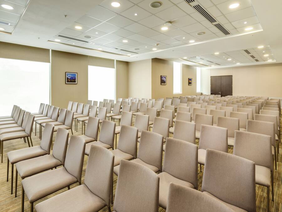A conference room with rows of beige chairs, large windows, and a carpeted floor.