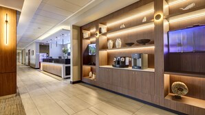 A modern hotel lobby with a reception desk, wooden shelving with decorative items, and a coffee machine. - Wyndham Santiago Aeropuerto (Santiago)